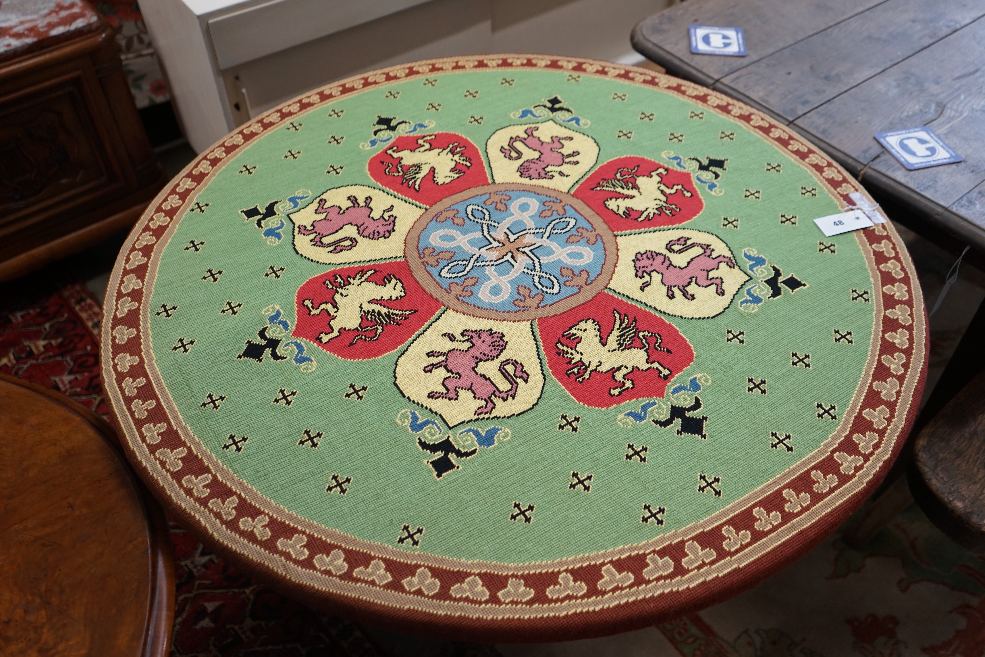 An early 20th century Continental carved oak circular centre table with heraldic tapestry top on winged lion supports, diameter 102cm, height 74cm